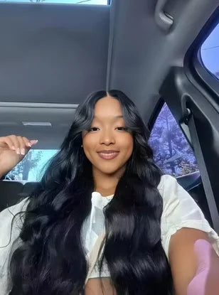 Woman with long black hair sitting inside a car, smiling.