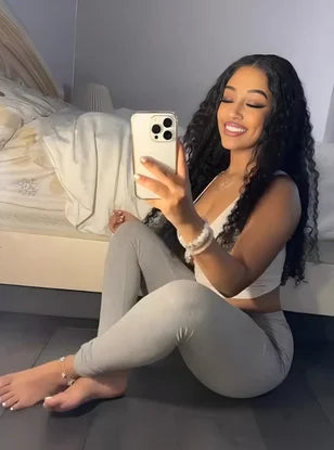 Woman taking a selfie in a sports bra and leggings on a bed.